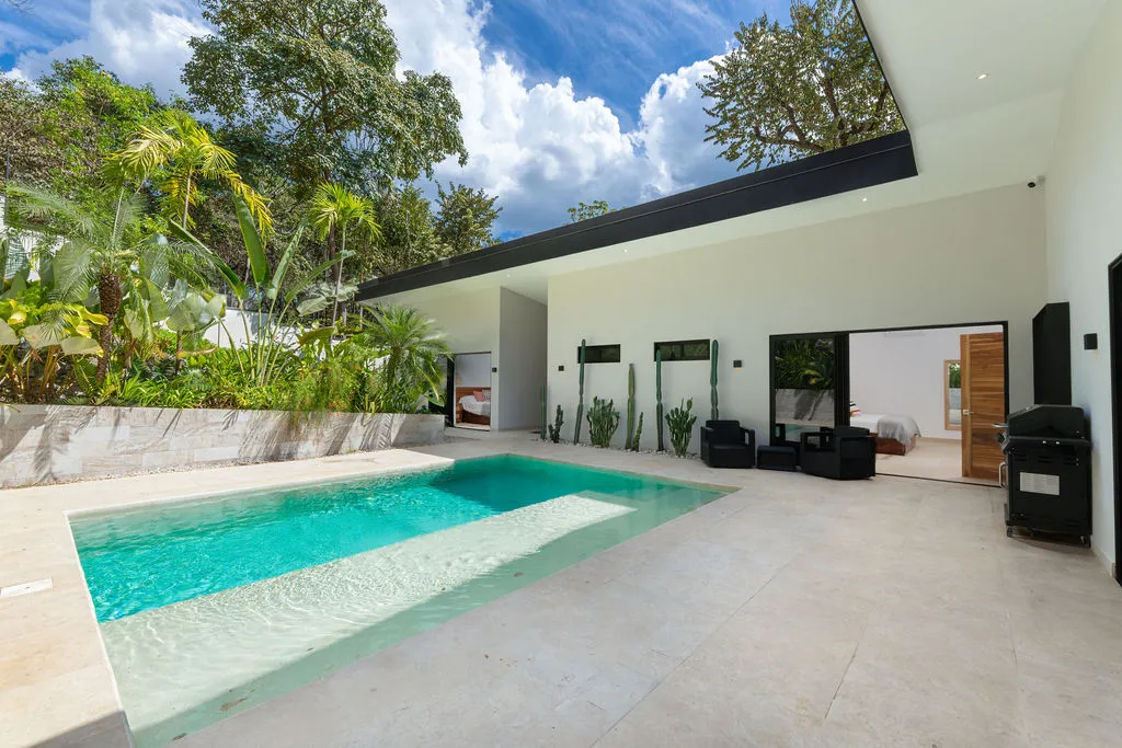 Turquoise pool bordered by tropical planting, with the living area open to the terrace behind it