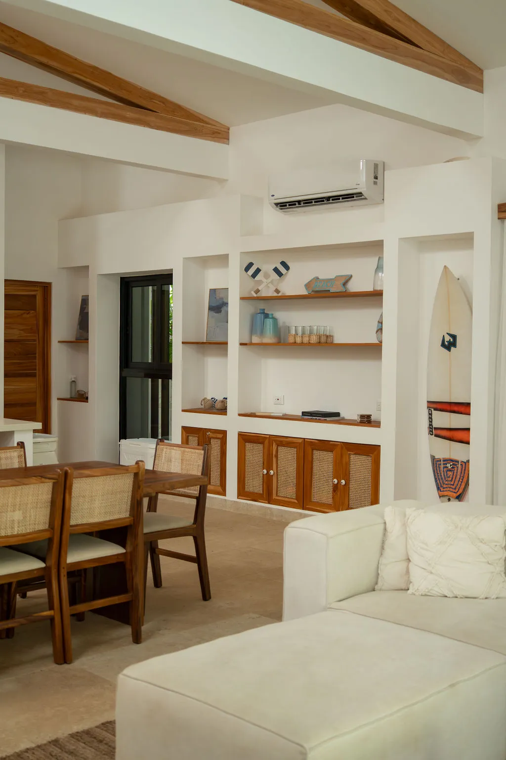 Living area with built-in shelving, a surfboard on the wall and a rattan dining set