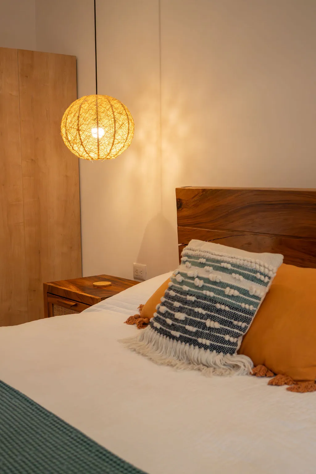 Bedroom with a solid wood headboard, woven pendant light and warm evening lighting
